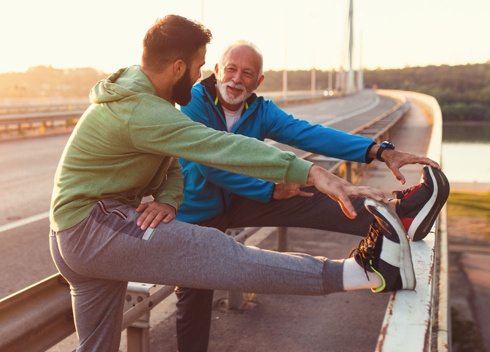 and older man stretching with a younger man after running.